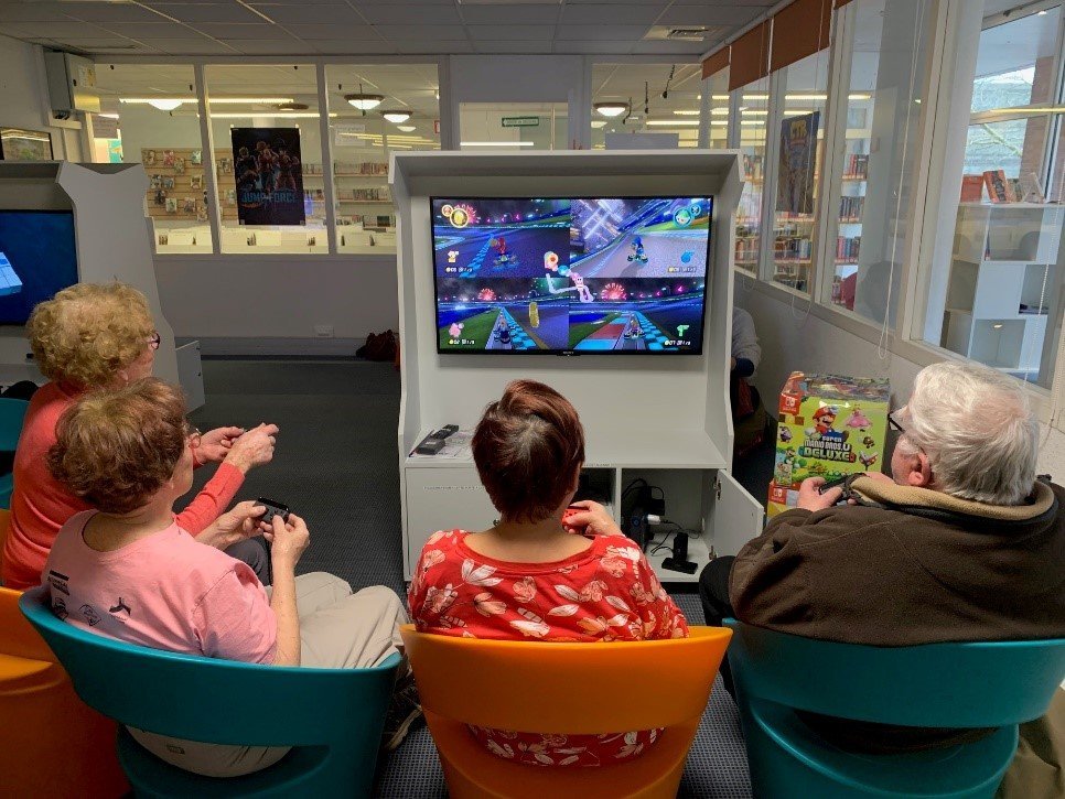 Photographie d'un groupe de trois seniors qui jouent assis à un jeu vidéo