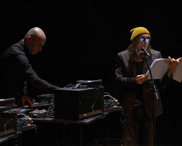 Le musicien Franck Vigroux règle des platines, à côté d'Eric Da Silva qui lit un texte sur scène. 