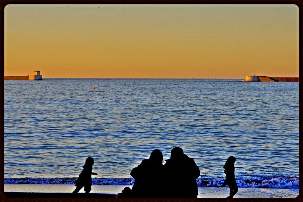 Photographie d'une plage sous un soleil couchant avec, en contre-jour, les silhouettes sombres de deux adultes et deux enfants