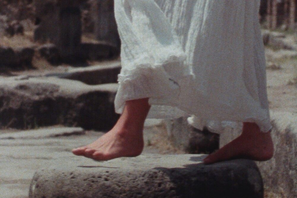 Des pieds nus, sortant d'une jupe blanche en mouvement, marchent sur une pierre.