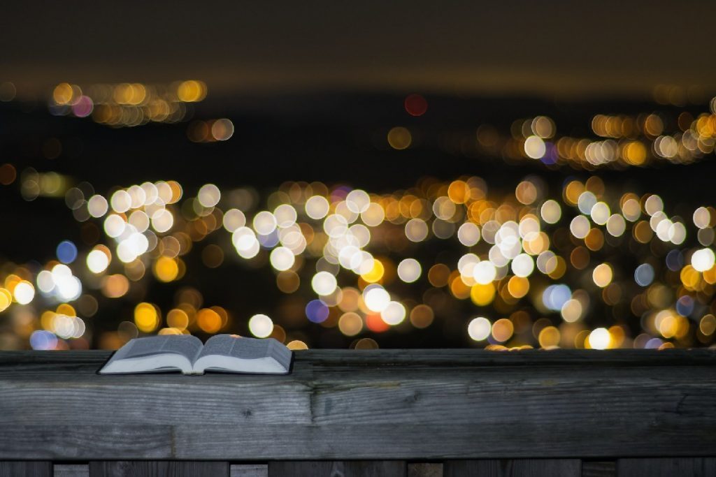 Un livre ouvert posé sur une rembarde en bois, avec les lumières d'une ville la nuit à l'arrière-plan