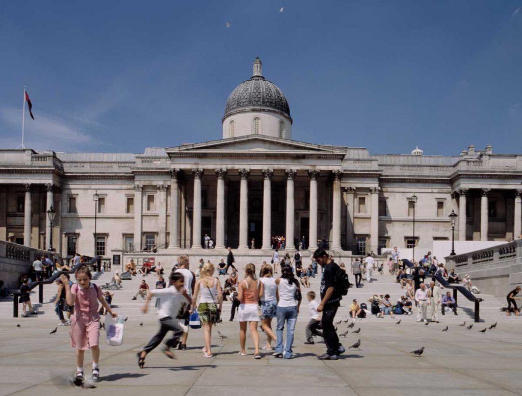 Des passants sur Trafalgar Square, devant l'escalier menant à la National Gallery de Londres