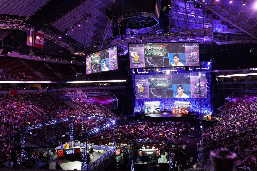 Un tournoi esport diffusé sur des écrans géantsdans une grande salle, avec un public nombreux.