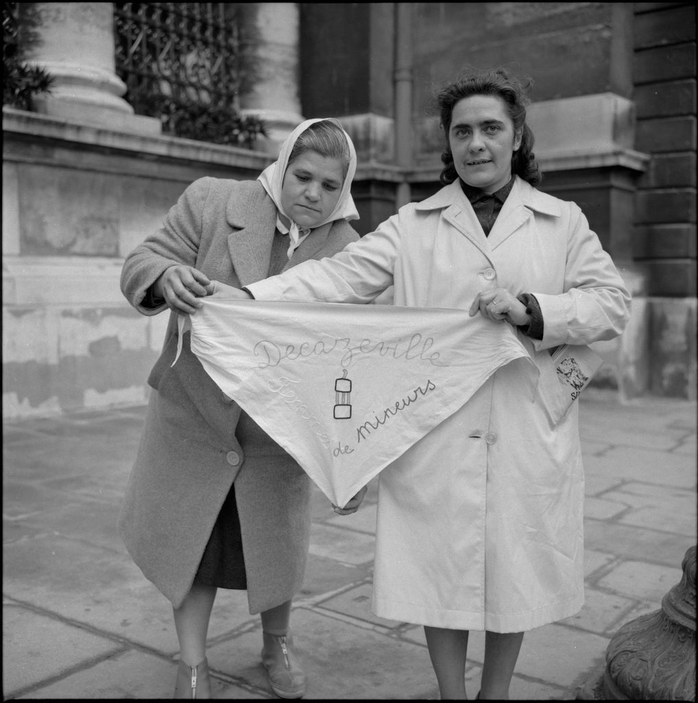 Deux femmes de mineurs de Decazeville en grève en janvier 1962. Elles déploient un foulard, orné de l'inscription « Decazeville femmes de mineurs ».