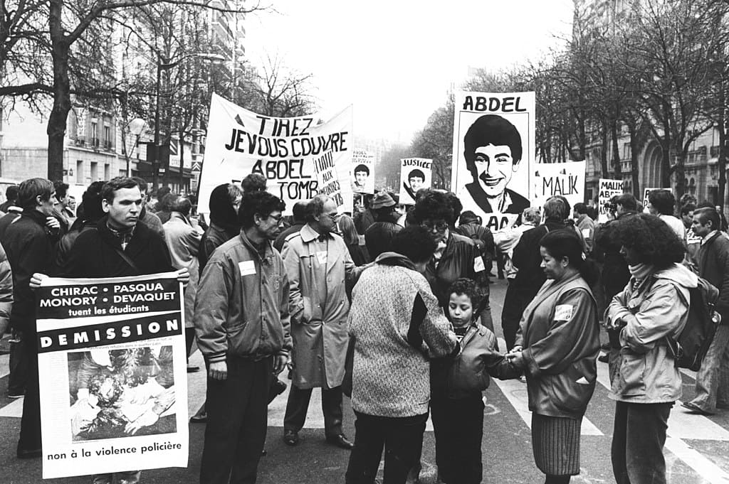 Des manifestants de tous âges tiennent des pancartes : "Tirez je vous couvre", "Chirac, Pasqua, Monory, Devaquet tuent des étudiants, démission".