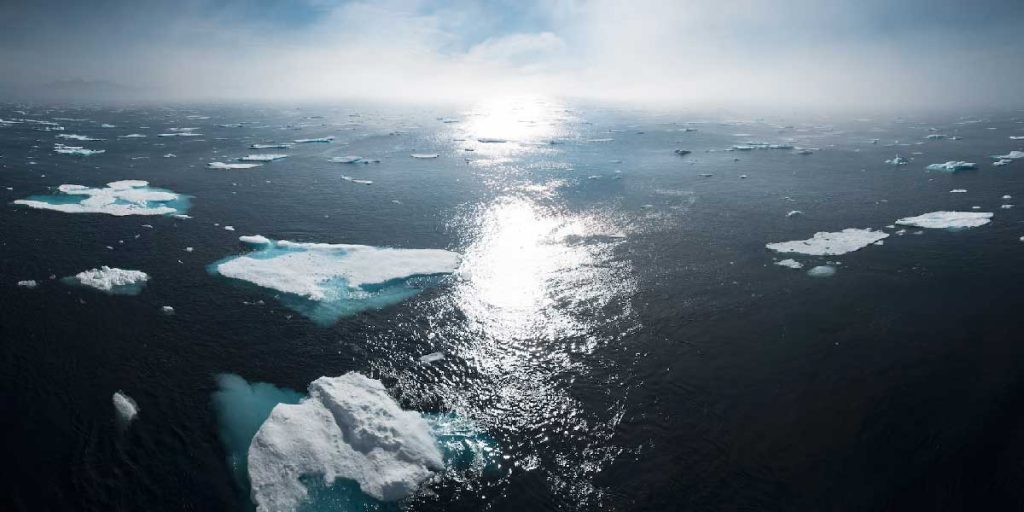 océan avec icebergs et soleil à l'horizon