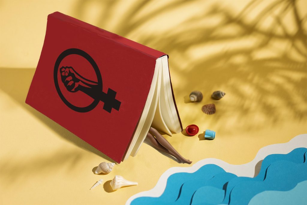 Un livre à la couverture rouge sur lequel figure un symbole féministe, sur une plage