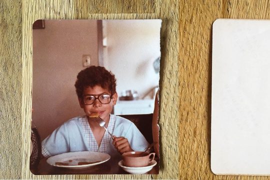 Sur une photo déchirée : un petit garçon avec des lunettes qui mange