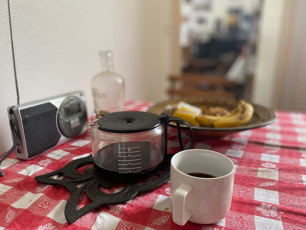 Sur la table d'une cuisine, des objets du quotidien (tasse à café, radio, cafetière...)