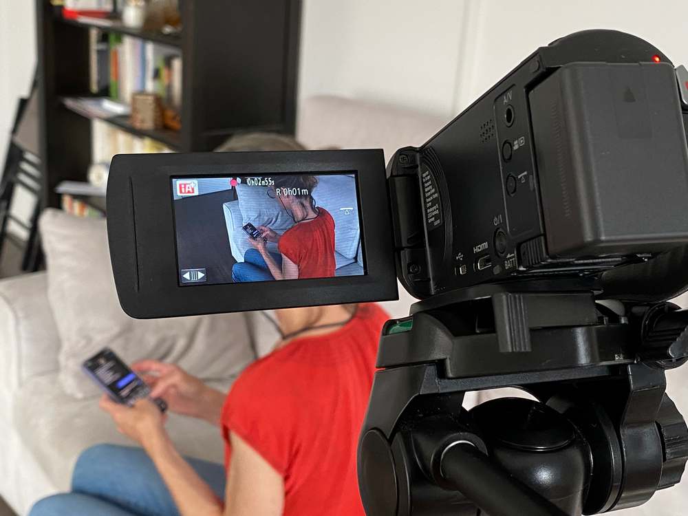 Une caméra est en train de filmer une femme de dos, assise sur son canapé, en train d'écrire un sms.