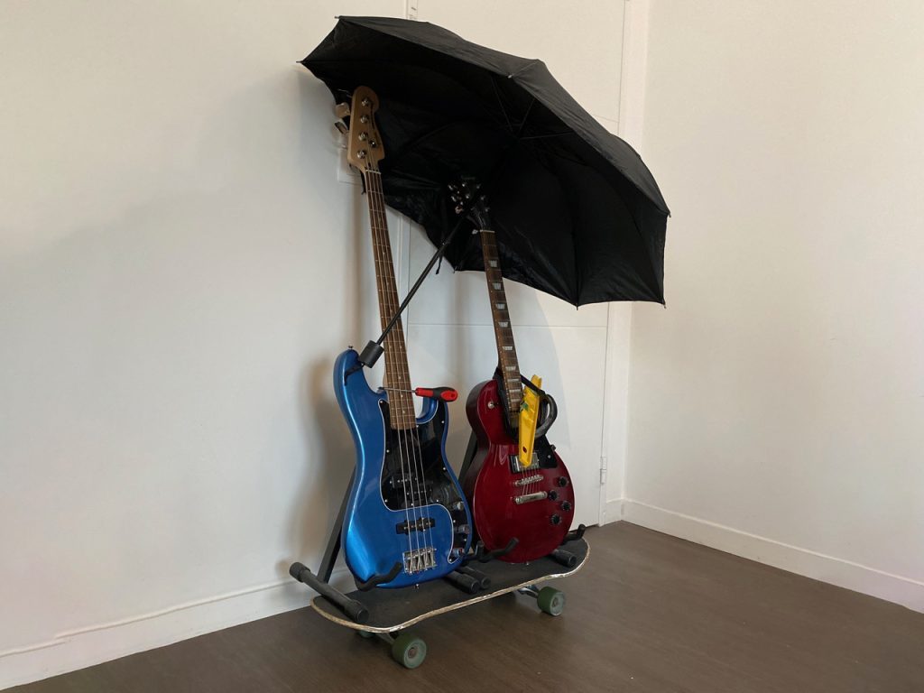 Une guitare et une basse sur un skate, protégées par un parapluie