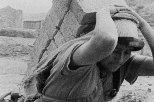 Une femme porte péniblement des briques sur son dos