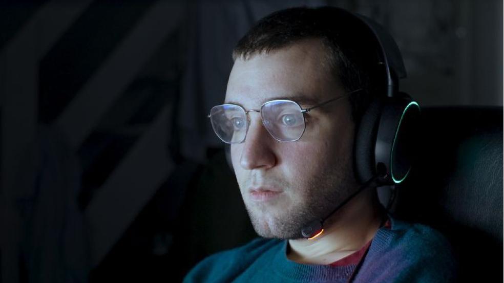 Un jeune homme porte un casque audio sur les oreilles, appuyé contre son siège de bureau, et fixe une source lumineuse