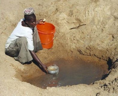 femme puisant de l'eau dans un trou au sol