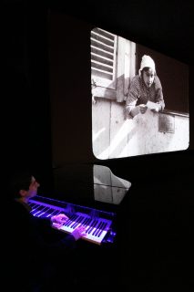 Photographie du pianiste Adelon Nisi en train d'accompagner un film muet qui passe à l'écran