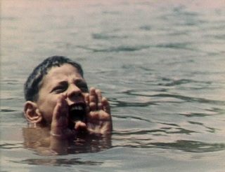 Photo d'un enfant plongé dans l'eau dont on ne voit que la tête, qui crie avec les mains en porte-voix