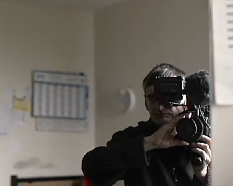 Denis Gheerbrant se filme dans un miroir, caméra à l'épaule.