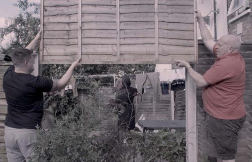 Scène : deux ouvriers montent une clôture dans le jardin du cinéaste