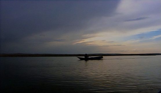 Image du film Déluge au pays du baas d'Omar Amiralay montrant un homme en barque sur le lac d'Assad