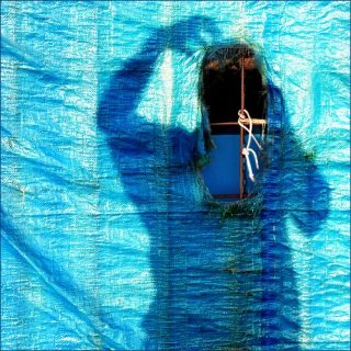L'ombre d'une personne sur une bâche bleue, qui se gratte la tête.