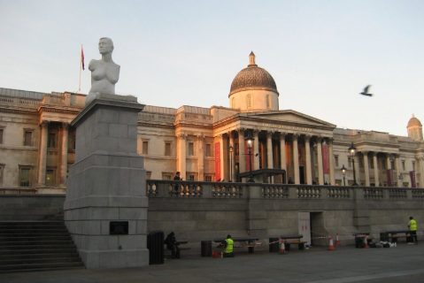Photographie de la National Gallery de Londres sous le soleil avec, au premier plan, une esplanade à l'ombre et, à gauche sur une colonne de pierre, une statue en marbre d'une femme sans bras