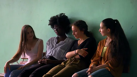Quatre adolescentes discutent, assises contre un mur.