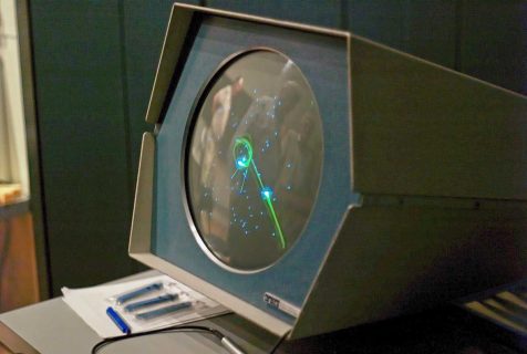 Un écran cathodique de mini ordinateur sur lequel les vaisseaux spatiaux du jeu Spacewar; sous forme de flèches, s'affrontent.
