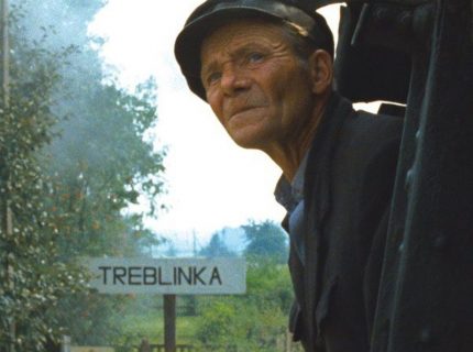 Un homme dans un train regard au loin, tandis qu'on aperçoit le panneau "Treblinka".