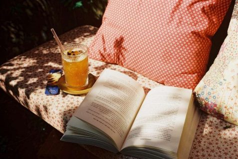 Un livre ouvert sur un banc posé à côté d'un verre de thé glacé