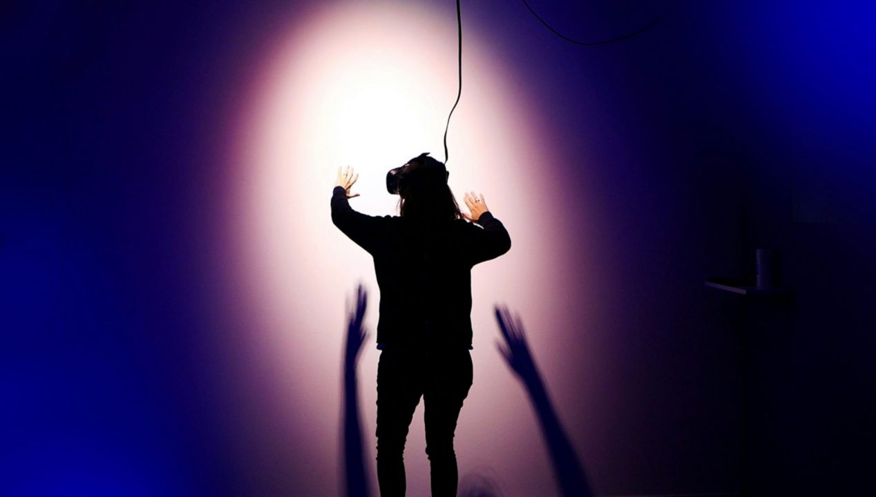 une personne de dos avec un casque virtuel sur les yeux fait face à un mur.