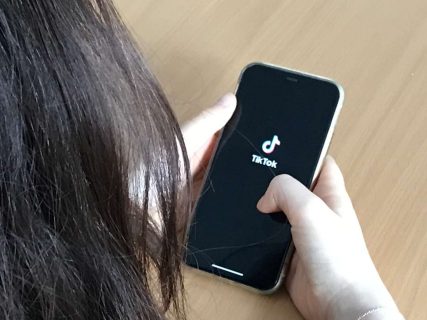 Gros plan sur des mains de femme manipulant son portable, sur lequel le logo de TikTok apparaît