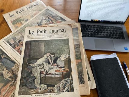 Exemplaires du quotidien Le Petit Journal près d'un ordinateur et d'un calpin noir