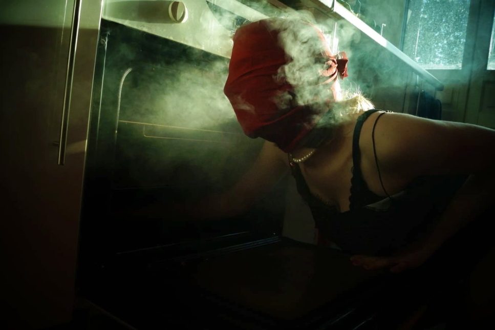 Jeune femme, dont le visage est masqué par un foulard rouge, dans un appartement sombre.