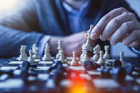 gros plan sur un plateau d'échecs. Une main déplace une pièce.