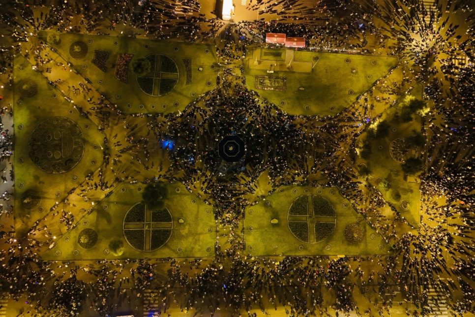 Vue aérienne d'une place, la nuit. des groupes de personnes rassemblées forment des motifs géométriques