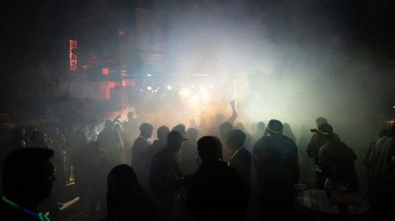 Des silouhettes dansent sur une piste de danse, au milieu d'un nuage de fumée.